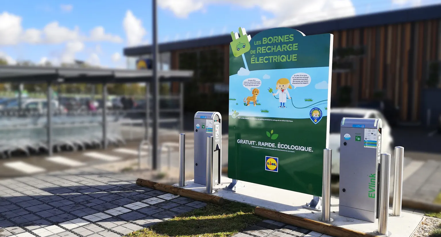 Panneau Lidl Les bornes de recharge électrique installé entre deux bornes sur le parking du magasin