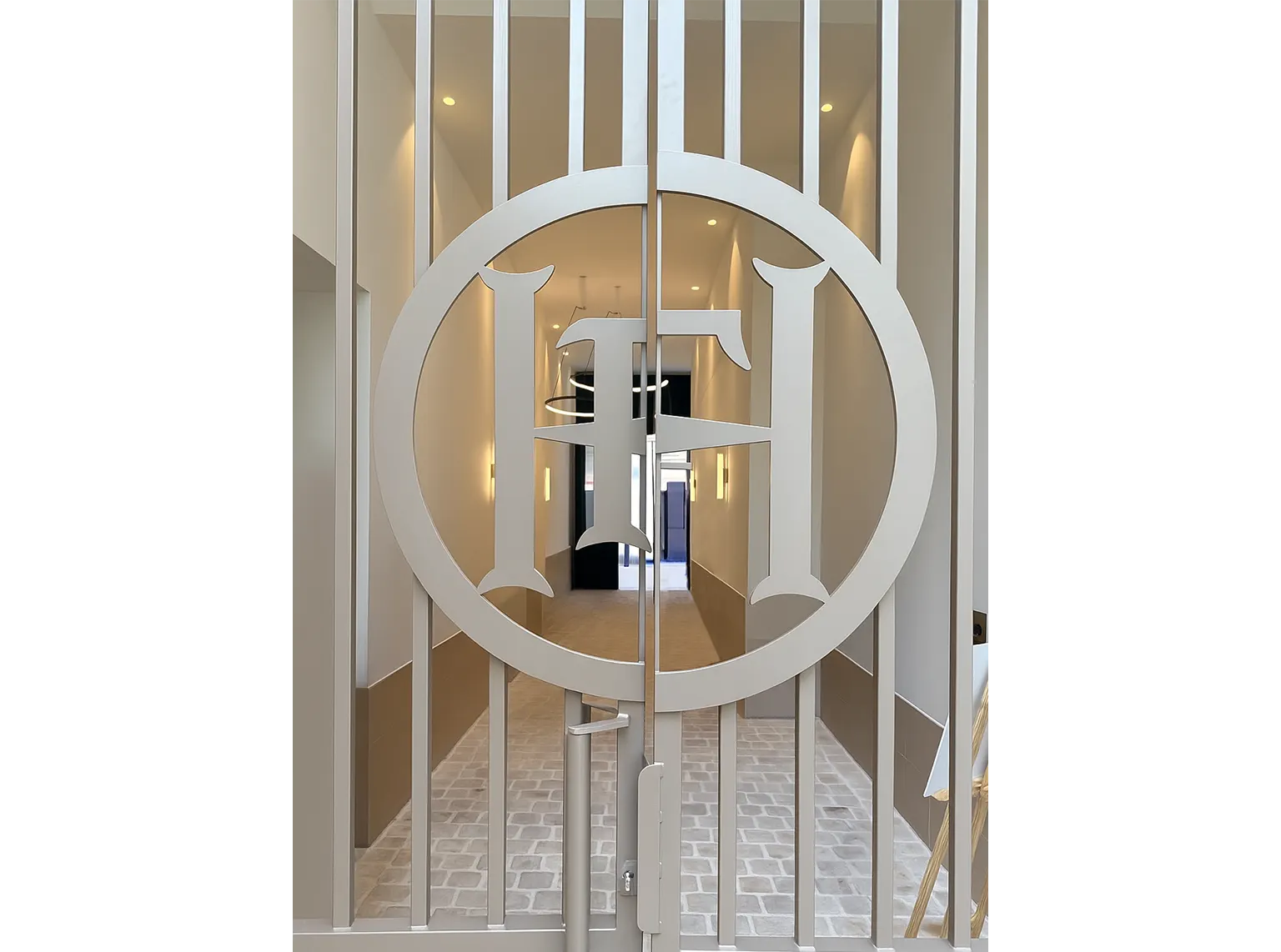Grille d'entrée de la résidence 133 FSH ornée du monogramme FH dans un cercle, ouvrant sur un hall lumineux